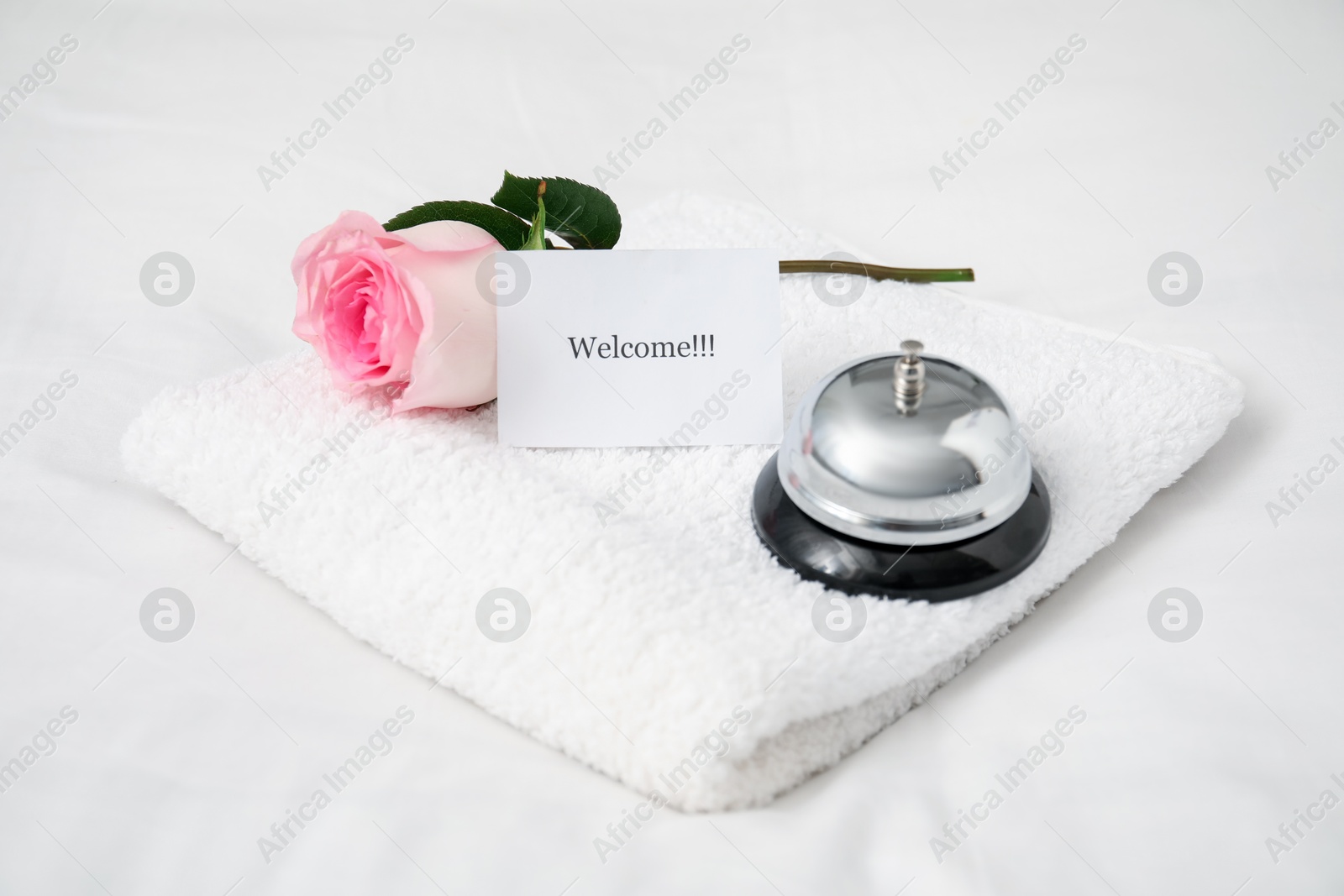Photo of Card with word Welcome, desk bell, rose and towel on white table