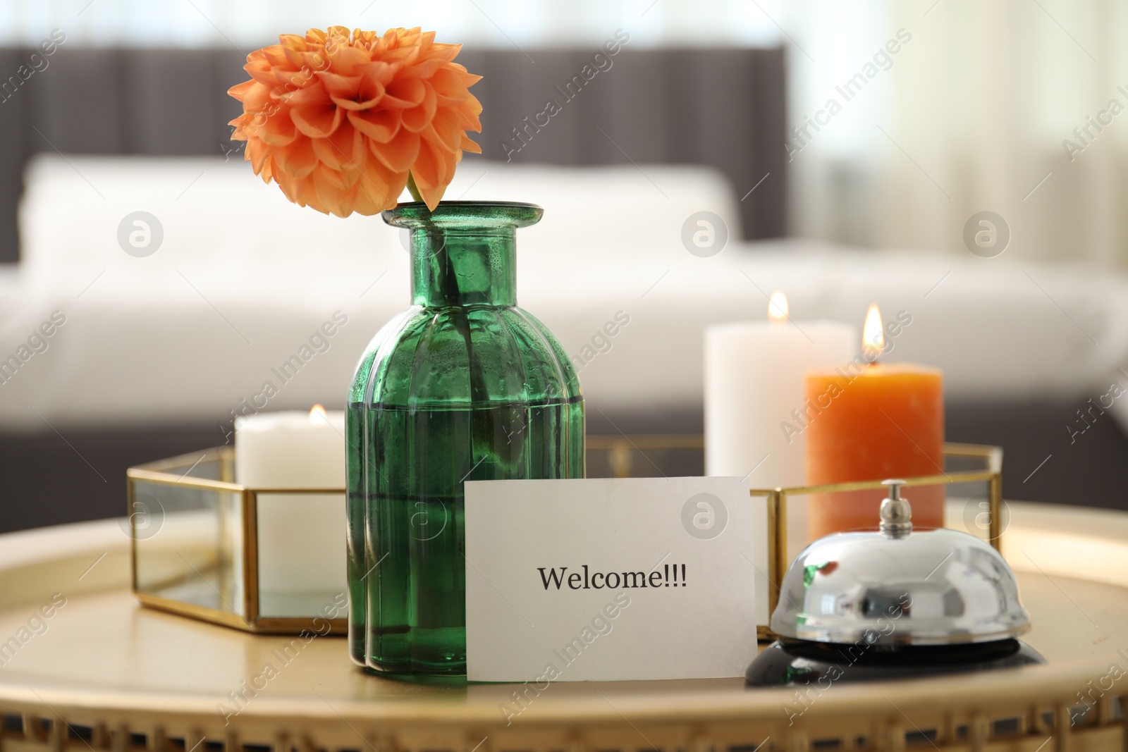 Card with word Welcome, desk bell, vase with flower and burning candles on table indoors Photo of Card with word Welcome, desk bell, vase with flower and burning candles on table indoors
