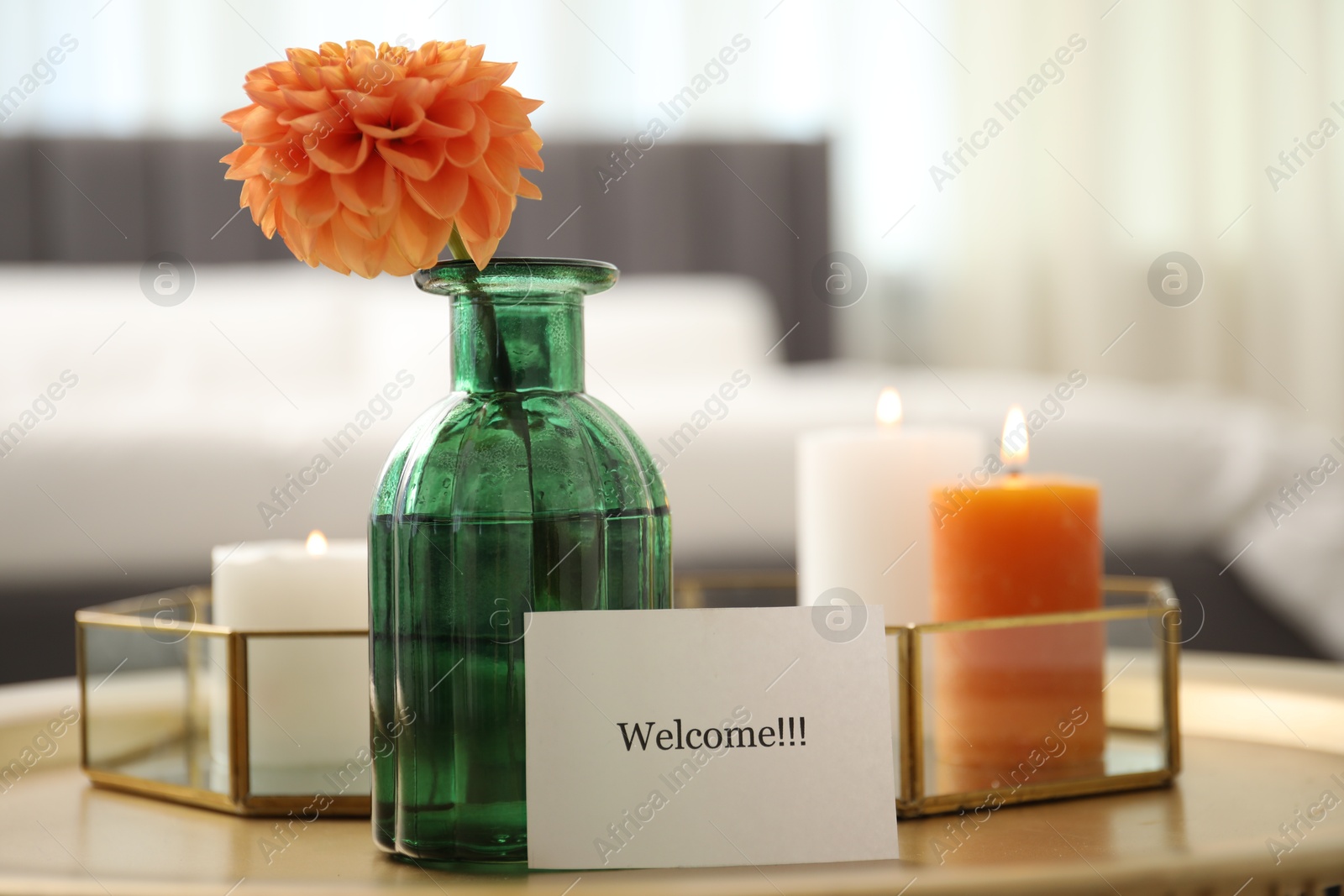 Photo of Card with word Welcome, vase with flower and burning candles on table indoors