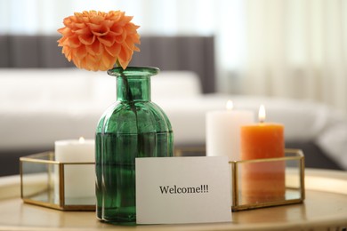 Photo of Card with word Welcome, vase with flower and burning candles on table indoors