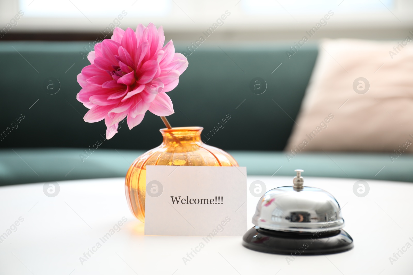 Photo of Card with word Welcome, desk bell and vase with flower on white table indoors