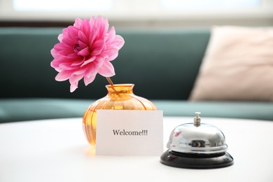 Photo of Card with word Welcome, desk bell and vase with flower on white table indoors
