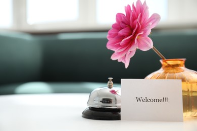 Photo of Card with word Welcome, desk bell and vase with flower on white table indoors. Space for text