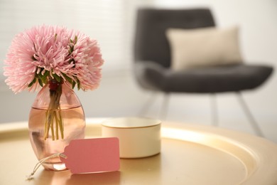 Photo of Blank card, vase with flowers and candle on table indoors. Space for text