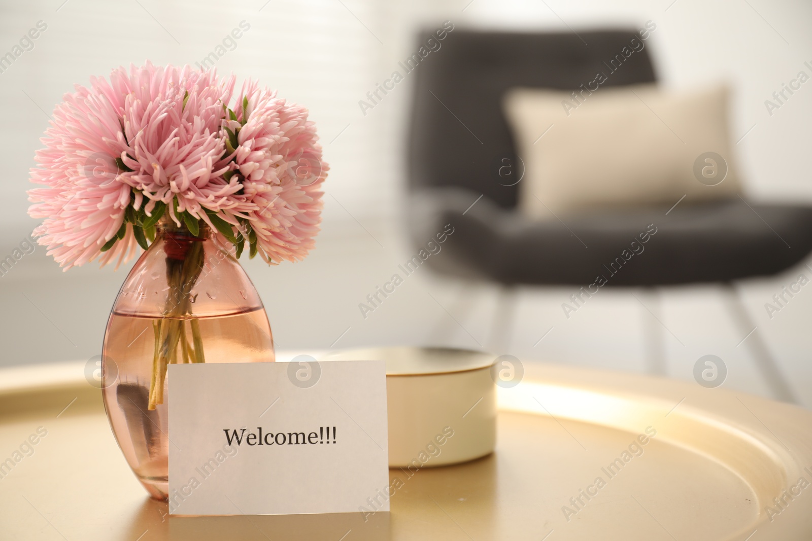 Photo of Card with word Welcome, candle and vase with flowers on table indoors, closeup. Space for text