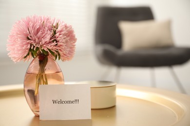 Photo of Card with word Welcome, candle and vase with flowers on table indoors, closeup. Space for text