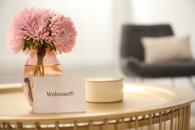 Photo of Card with word Welcome, candle and vase with flowers on table indoors, closeup. Space for text