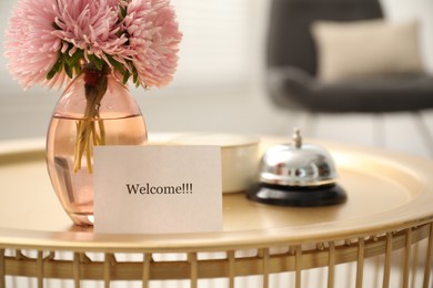 Photo of Card with word Welcome, desk bell, candle and vase with flowers on table indoors, closeup