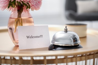 Photo of Card with word Welcome, desk bell, candle and vase with flowers on table indoors, closeup
