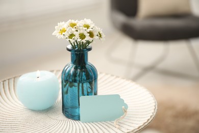 Photo of Blank card, vase with flowers and candle on table indoors. Space for text
