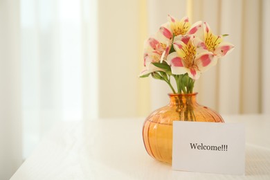 Photo of Card with word Welcome and vase with flowers on white table indoors. Space for text