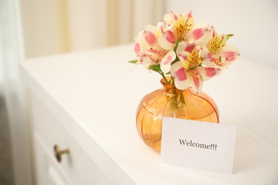 Photo of Card with word Welcome and vase with flowers on white table indoors. Space for text