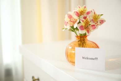 Photo of Card with word Welcome and vase with flowers on white table indoors. Space for text