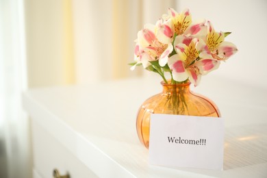 Photo of Card with word Welcome and vase with flowers on white table indoors. Space for text