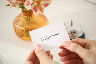 Photo of Woman holding card with word Welcome indoors, closeup
