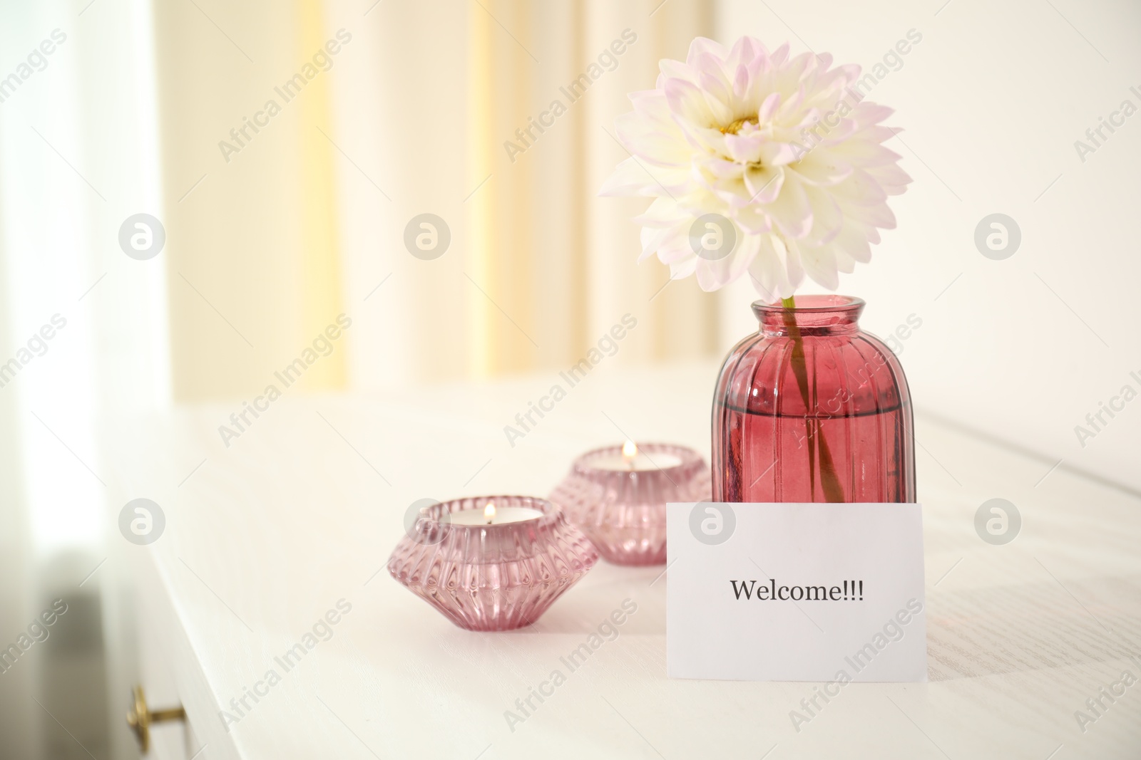 Photo of Card with word Welcome, vase with flower and candles on white table indoors. Space for text