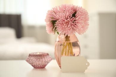 Photo of Blank card, vase with flowers and candle on white table indoors
