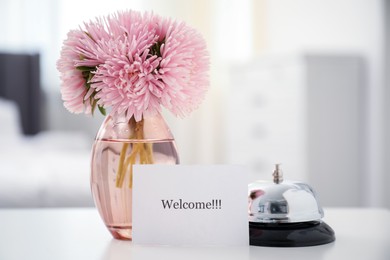 Photo of Card with word Welcome, desk bell and vase with flowers on white table indoors. Space for text