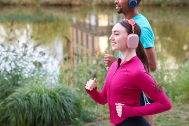 Photo of Smiling couple in headphones running near river outdoors, closeup. Space for text