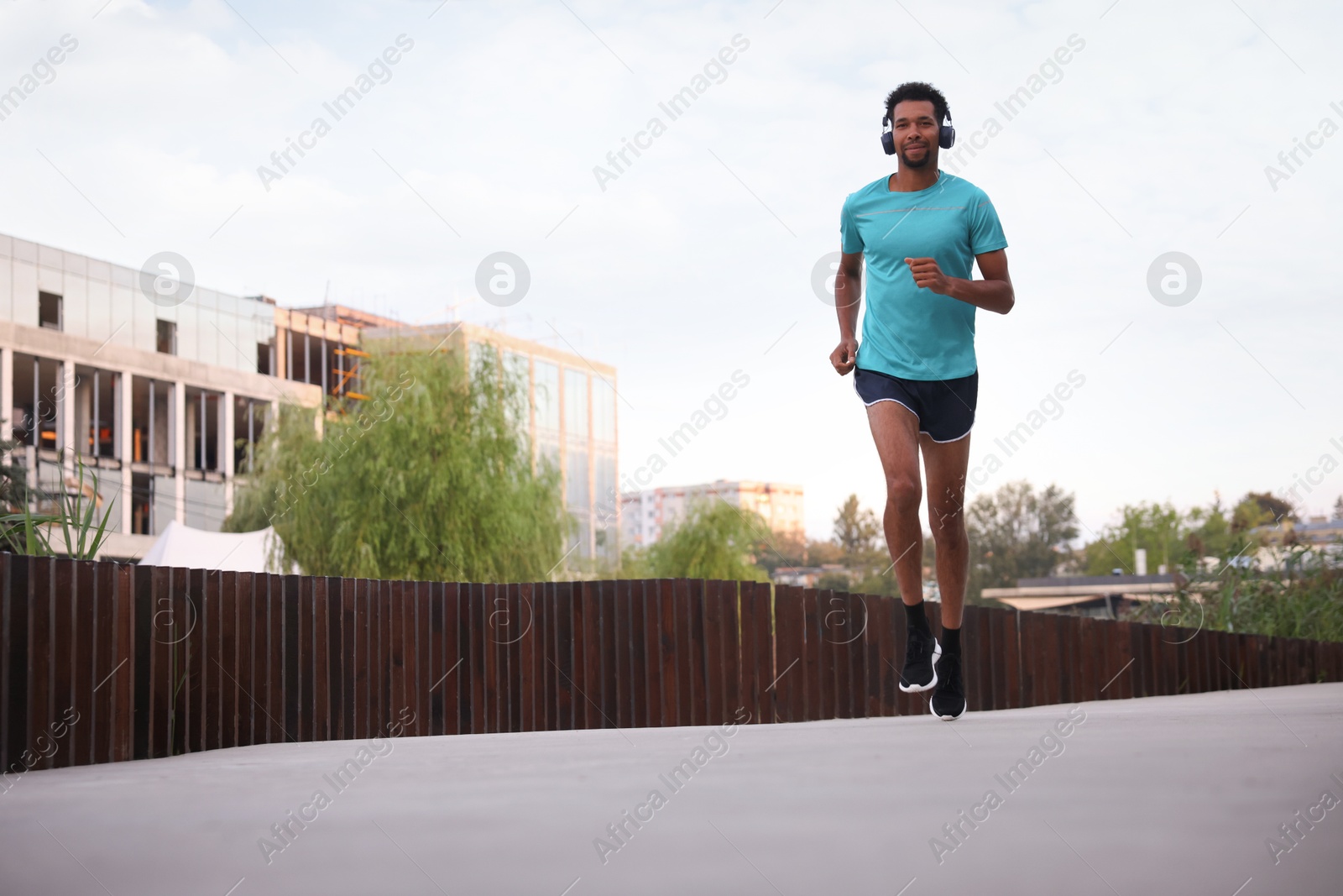 Photo of Handsome man in headphones running outdoors, low angle view. Space for text