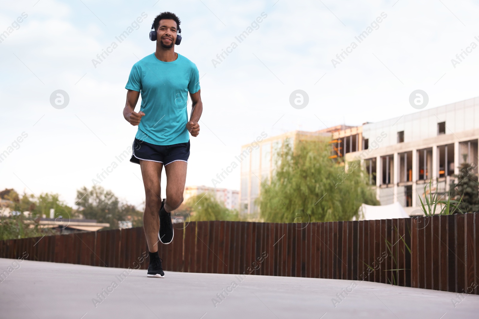 Photo of Handsome man in headphones running outdoors, low angle view. Space for text