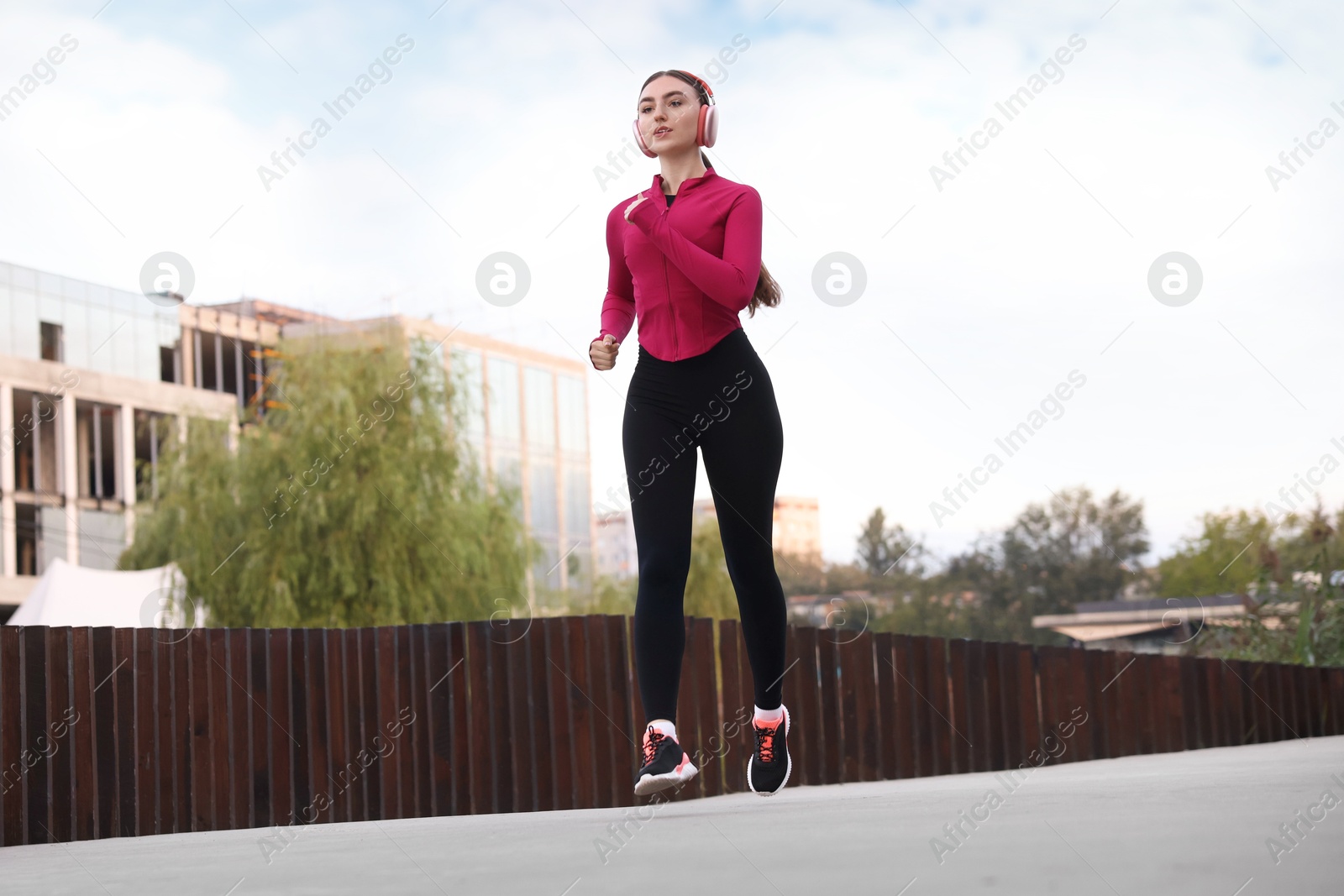 Photo of Beautiful woman in headphones running outdoors, low angle view