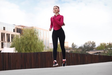 Photo of Beautiful woman in headphones running outdoors, low angle view
