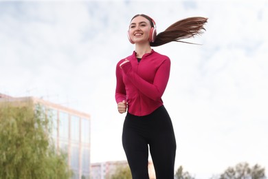 Photo of Smiling woman in headphones running outdoors, low angle view