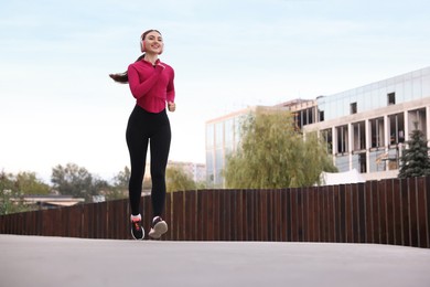 Photo of Smiling woman in headphones running outdoors, low angle view. Space for text