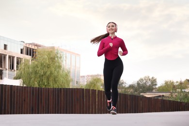 Photo of Smiling woman in headphones running outdoors, low angle view. Space for text