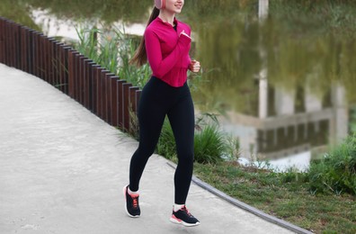 Photo of Smiling woman in sportswear running near river outdoors, closeup