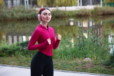 Photo of Smiling woman in headphones running near river outdoors. Space for text