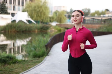 Photo of Smiling woman in headphones running near river outdoors. Space for text