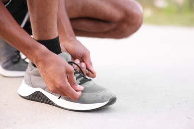 Photo of Runner tying shoelace of his sneaker outdoors, closeup. Space for text