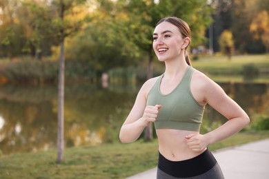 Photo of Smiling woman in sportswear running outdoors. Space for text