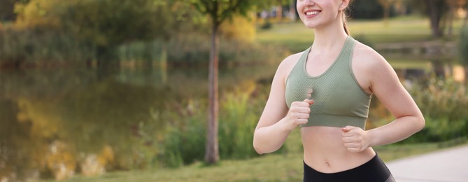 Photo of Smiling woman in sportswear running outdoors, closeup. Space for text