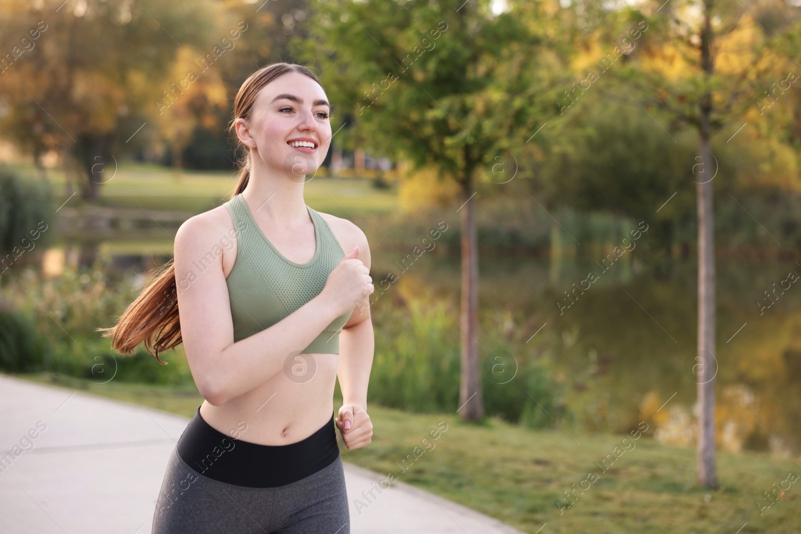 Photo of Smiling woman in sportswear running outdoors. Space for text