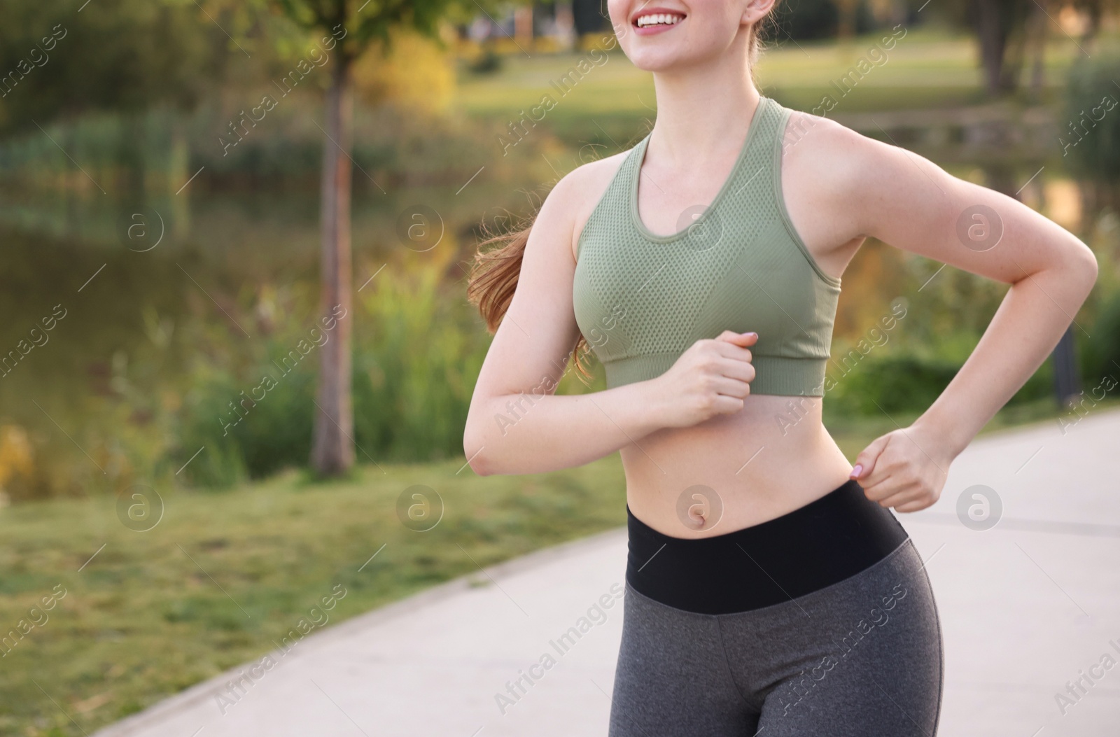 Photo of Smiling woman in sportswear running outdoors, closeup. Space for text