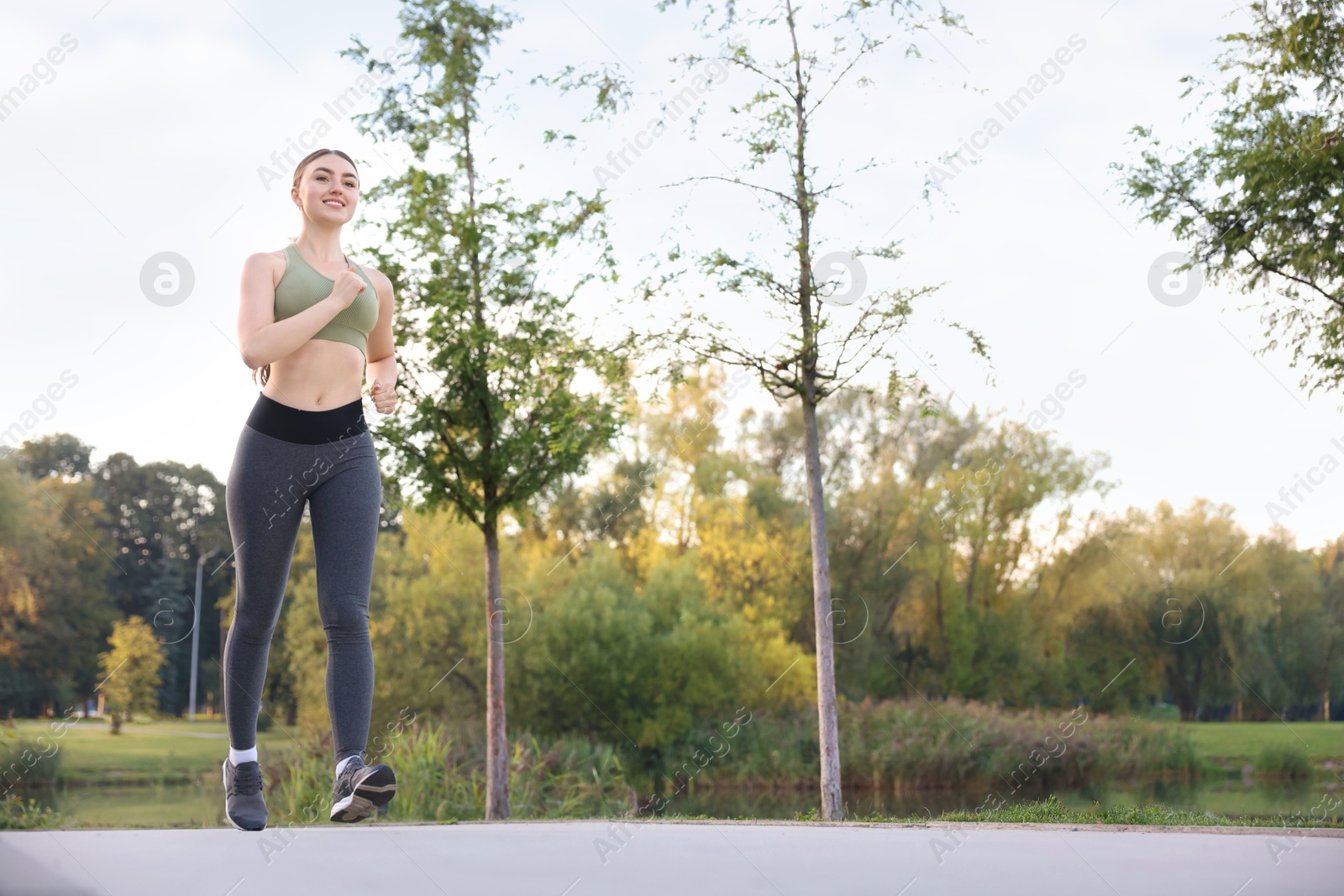 Photo of Smiling woman in sportswear running outdoors, low angle view. Space for text
