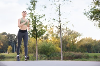 Photo of Smiling woman in sportswear running outdoors, low angle view. Space for text