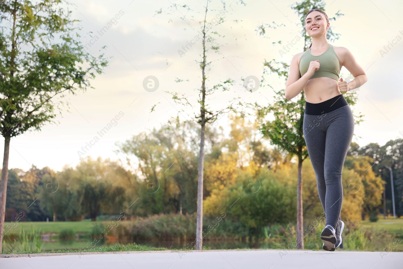 Photo of Smiling woman in sportswear running outdoors, low angle view. Space for text