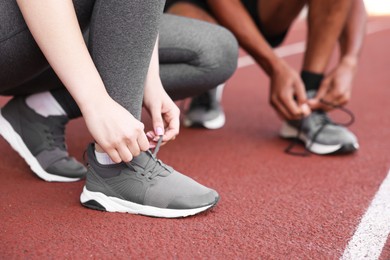 Photo of Runners tying shoelaces of their sneakers at stadium, closeup
