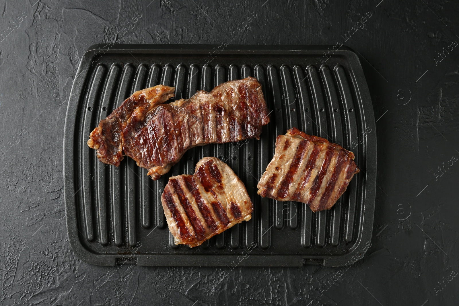 Photo of Delicious grilled beef meat on black textured table, top view