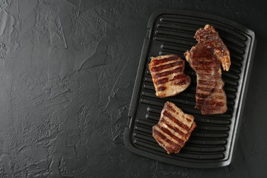 Photo of Delicious grilled beef meat on black textured table, top view. Space for text
