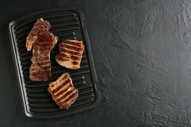 Photo of Delicious grilled beef meat on black textured table, top view. Space for text