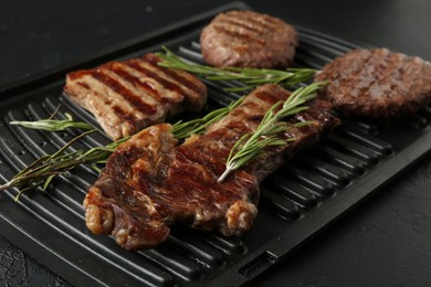 Photo of Delicious grilled beef meat with rosemary on black textured table, closeup