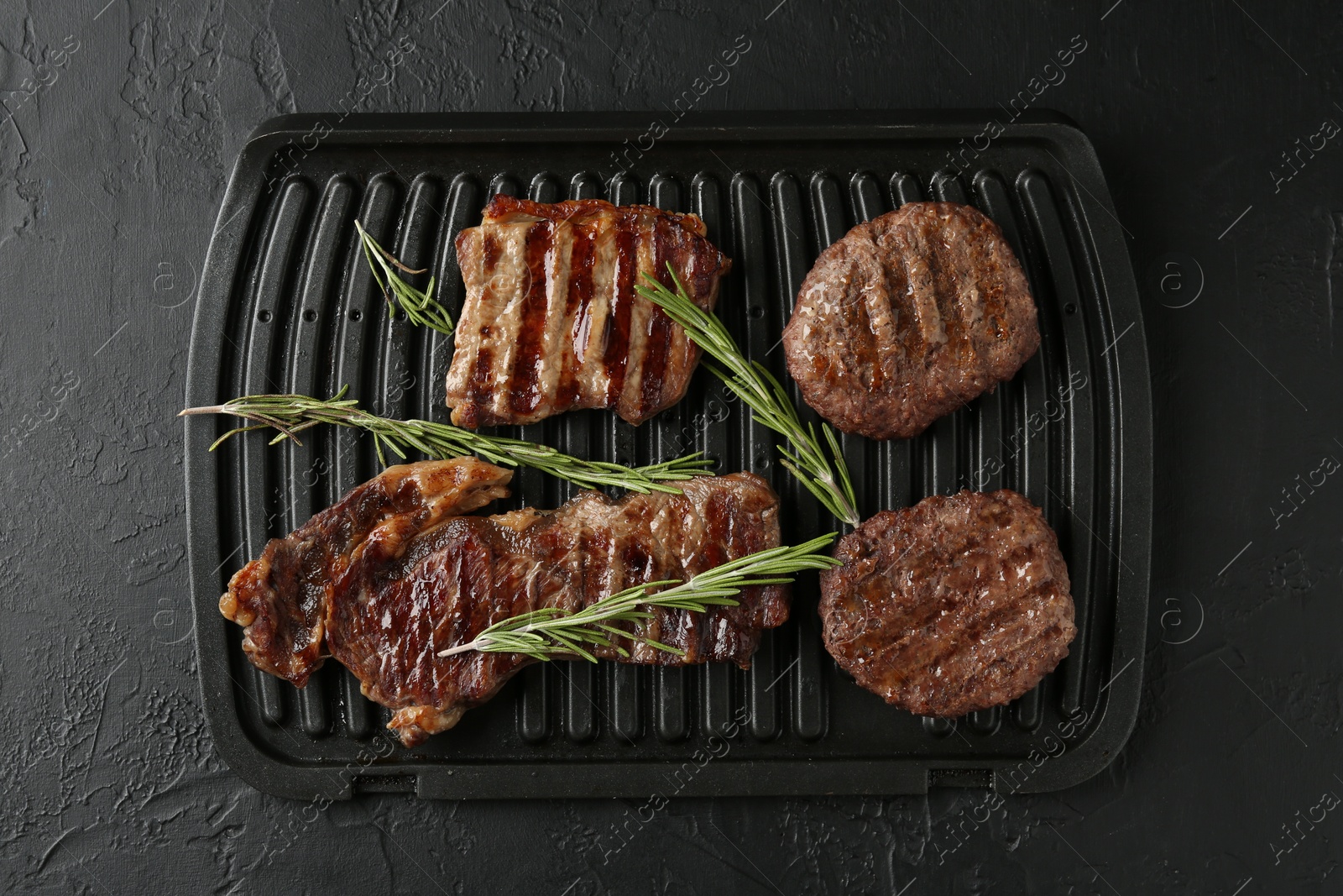 Photo of Delicious grilled beef meat with rosemary on black textured table, top view