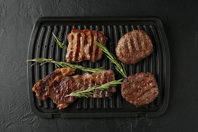 Photo of Delicious grilled beef meat with rosemary on black textured table, top view