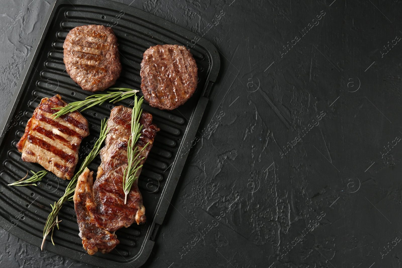 Photo of Delicious grilled beef meat with rosemary on black textured table, top view. Space for text