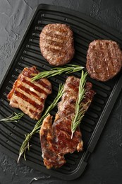 Photo of Delicious grilled beef meat with rosemary on black textured table, top view